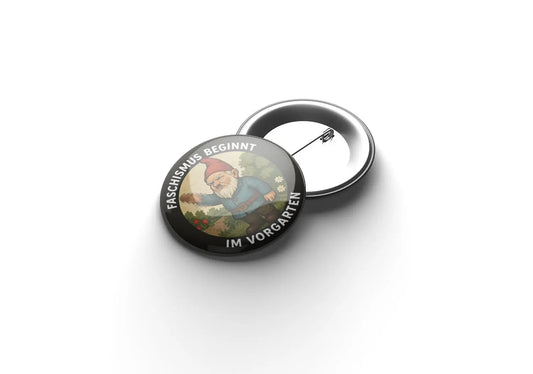 „Runder Button mit schwarzem Rand und weißer Aufschrift ‚Faschismus beginnt im Vorgarten‘; in der Mitte steht ein gezeichneter Gartenzwerg mit roter Mütze und blauer Jacke in einer Gartenlandschaft.“