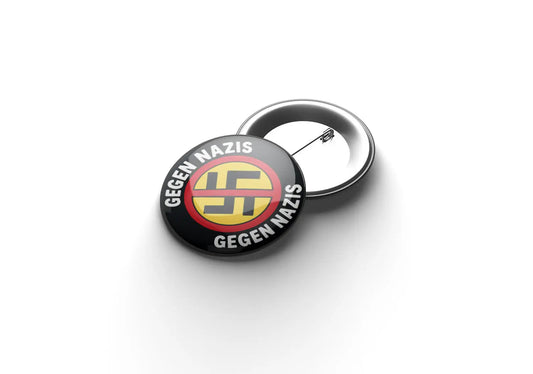 „Runder Button mit schwarzem Hintergrund und weißer Aufschrift ‚GEGEN NAZIS‘ oben und unten; in der Mitte ein gelber Kreis mit rotem Rand und einem durchgestrichenen schwarzen Symbol.“