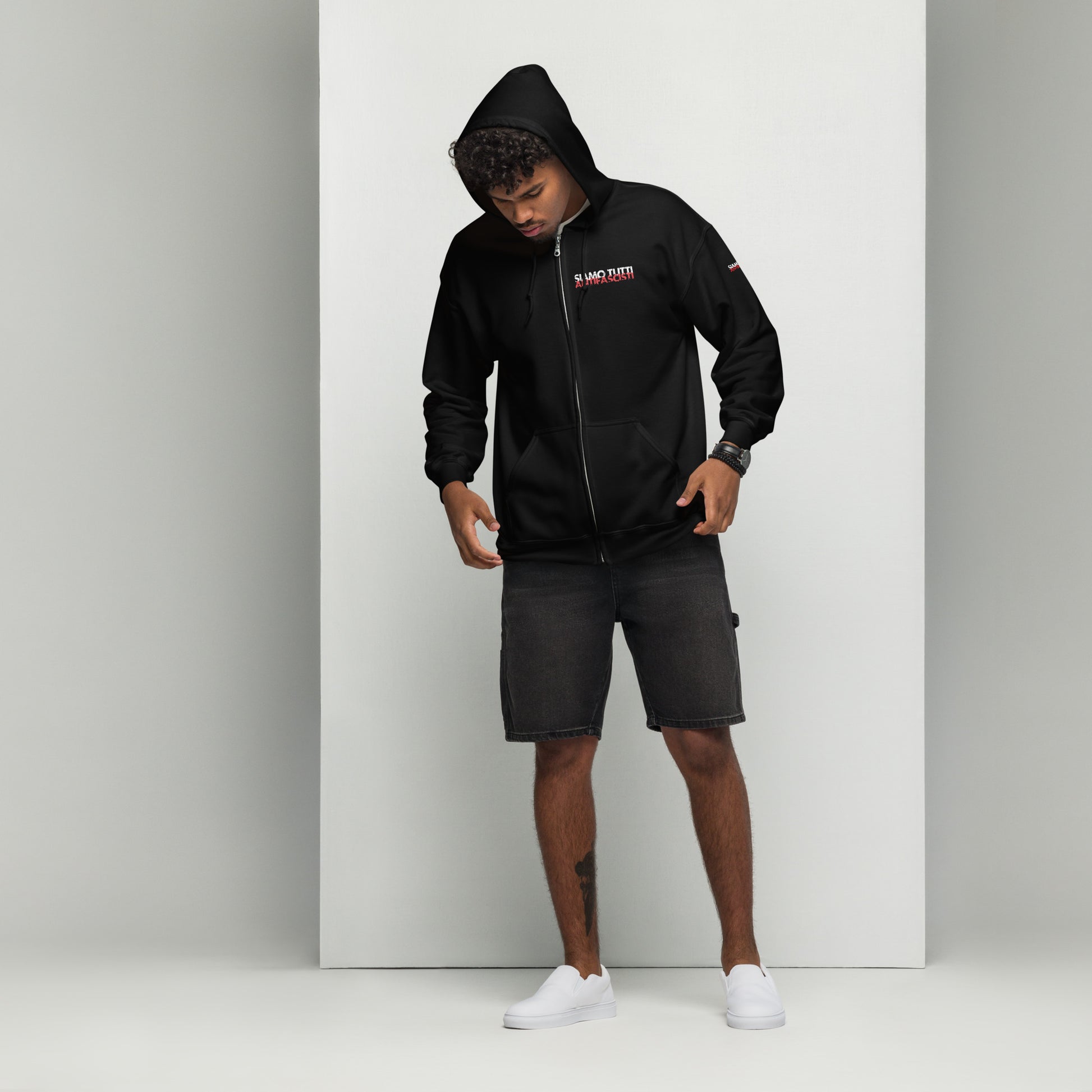 „Person trägt schwarzen Zip‑Hoodie mit Kapuze und Brustprint ‚NO PAIN NO GAIN‘ in Weiß und Rot, kombiniert mit schwarzen Shorts und weißen Slippern – sportlich-lässiger Streetwear-Look vor hellem Hintergrund.“