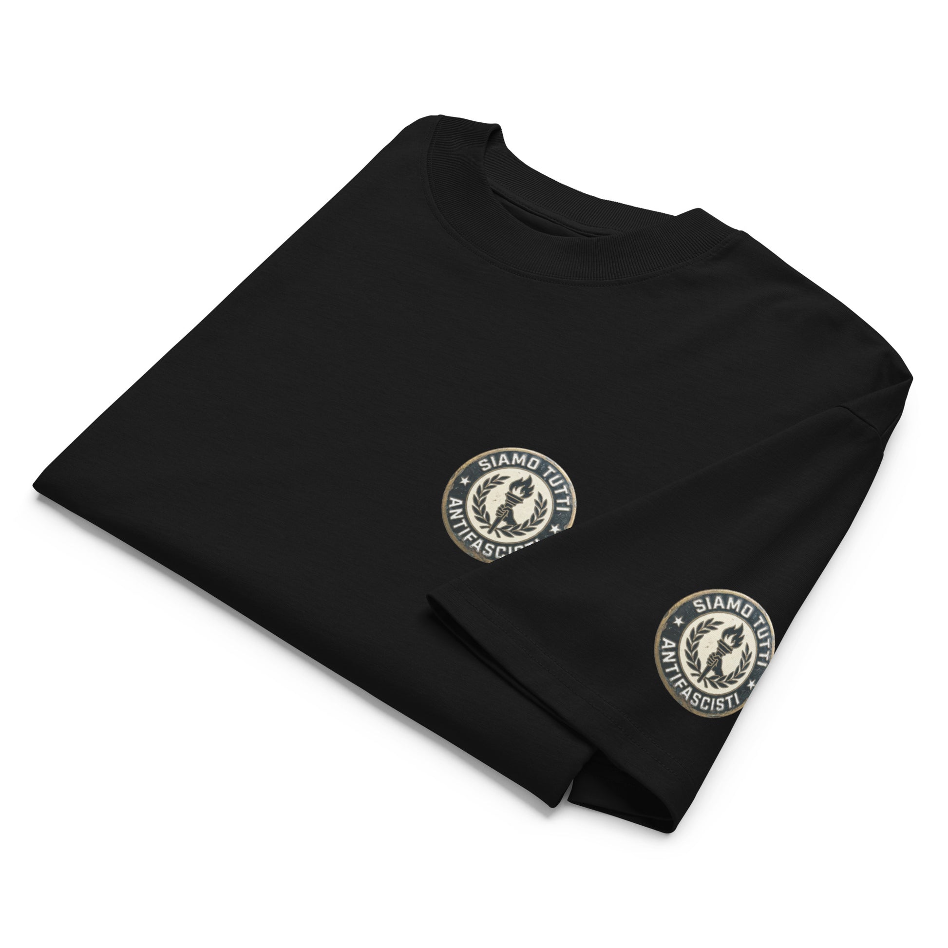 Schwarzes Oversize‑T‑Shirt mit zwei runden Emblem‑Logos auf Brust und Ärmel. Detailansicht.