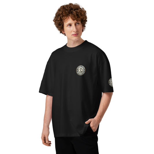 Schwarzes Oversize‑T‑Shirt mit zwei runden Logos auf Brust und Ärmel, jeweils mit stilisiertem Emblem und umlaufendem Schriftzug.
